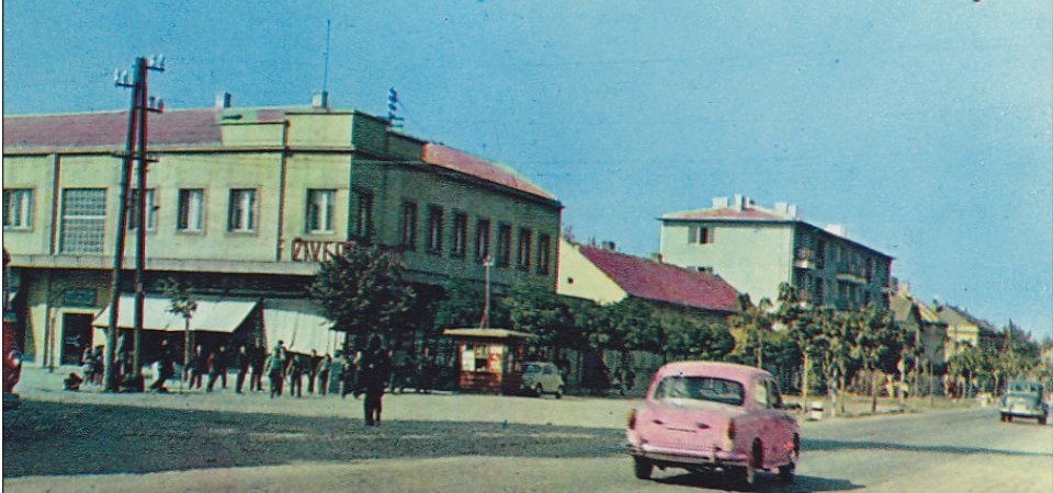 Na staroj fotografiji s druge polovine 20. veka vidi se centar Stare Pazove, ljudi, automobili, kombi, sa leve strane je zelena zgrada nekadašnjeg Cetrotekstila.