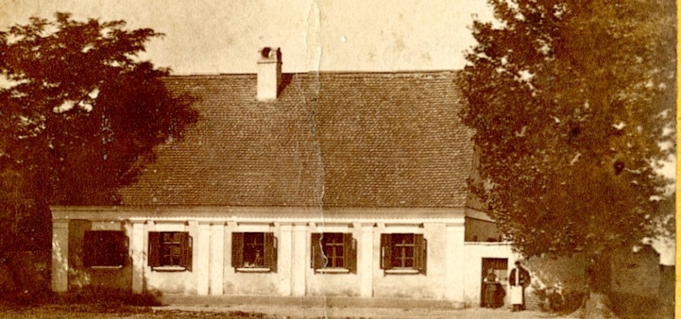 Na staroj fotografiji s druge polovine 19. veka vidi se parohijski dom evangeličke crkve, drveće, muskarac i žena stoje ispred kapije.